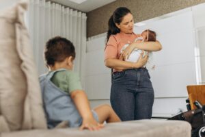 Mother Standing with Baby and Son Sitting near